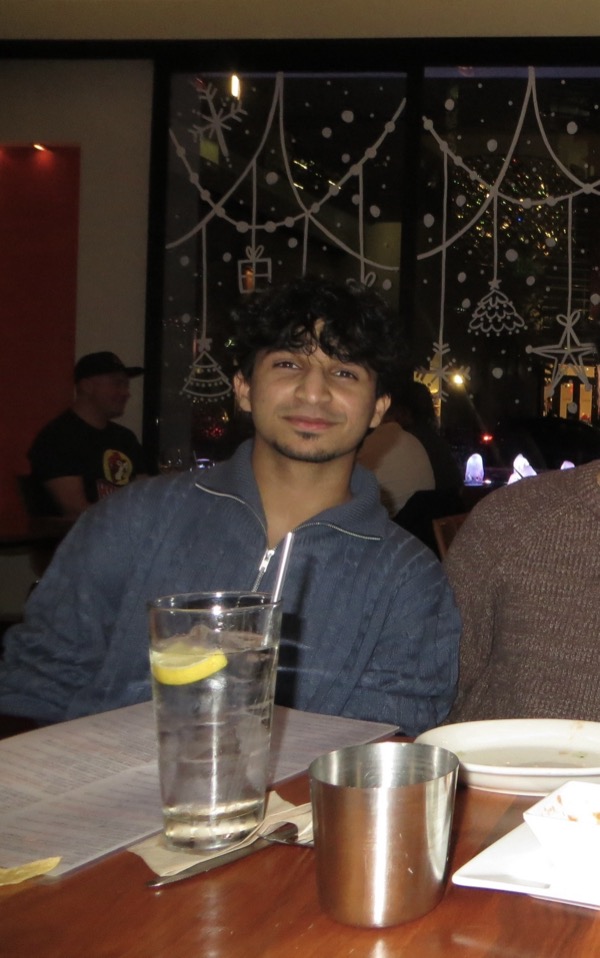Madhav Suri smiling at a restaurant table with string-light window decorations behind him